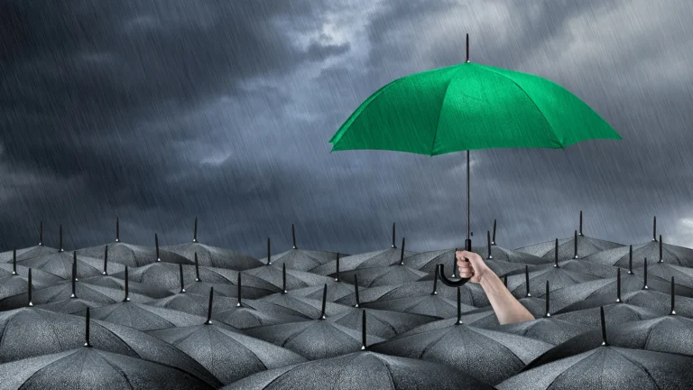 A green umbrella stands out in a sea of black ones during a storm, symbolizing hope and standing strong amid adversity.