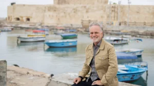 Tony Sarsam on a stone causeway in Alexandria's eastern harbor, with the Citadel of Qaitbay — built on the foundations of the lost Pharos lighthouse — behind him