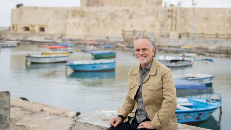 Tony Sarsam on a stone causeway in Alexandria's eastern harbor, with the Citadel of Qaitbay — built on the foundations of the lost Pharos lighthouse — behind him